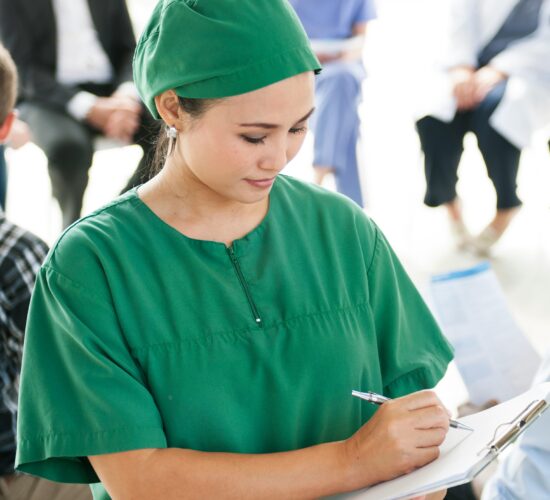 Female physician in green scrubs writing notes during a community healthcare or philanthropy event.