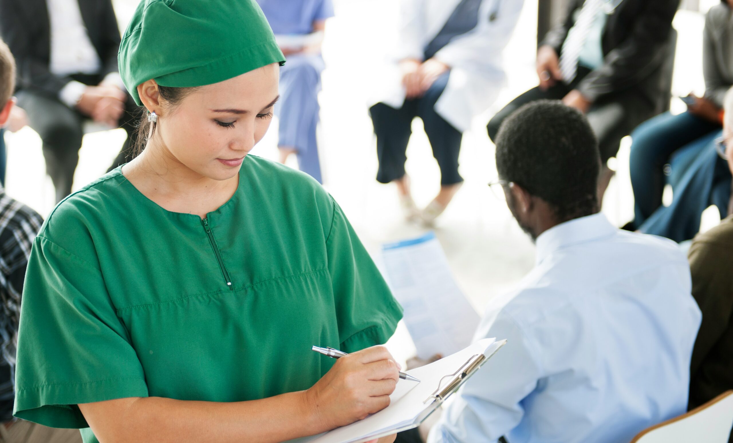 Female physician in green scrubs writing notes during a community healthcare or philanthropy event.